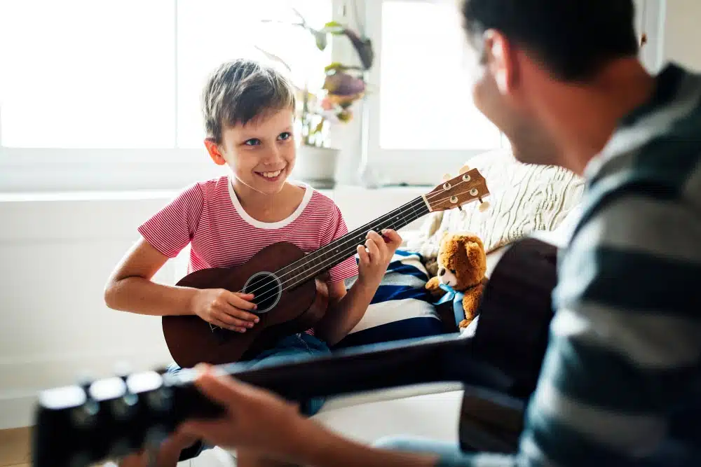 Professeur de guitar offrant un cours de musique à un enfant. L'enfant sourit, car sont prof rend l'apprentissage de la musique amusant